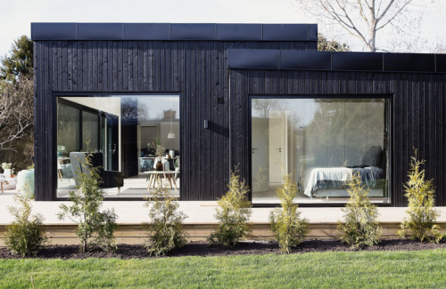 Modernes Haus aus dunklem Holz mit großen Aluminium-Fenstern.