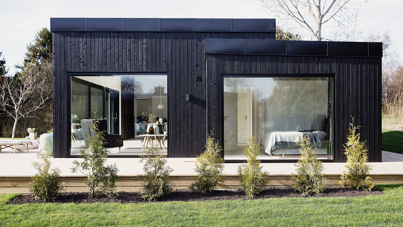 Modernes Haus aus dunklem Holz mit großen Aluminium-Fenstern.