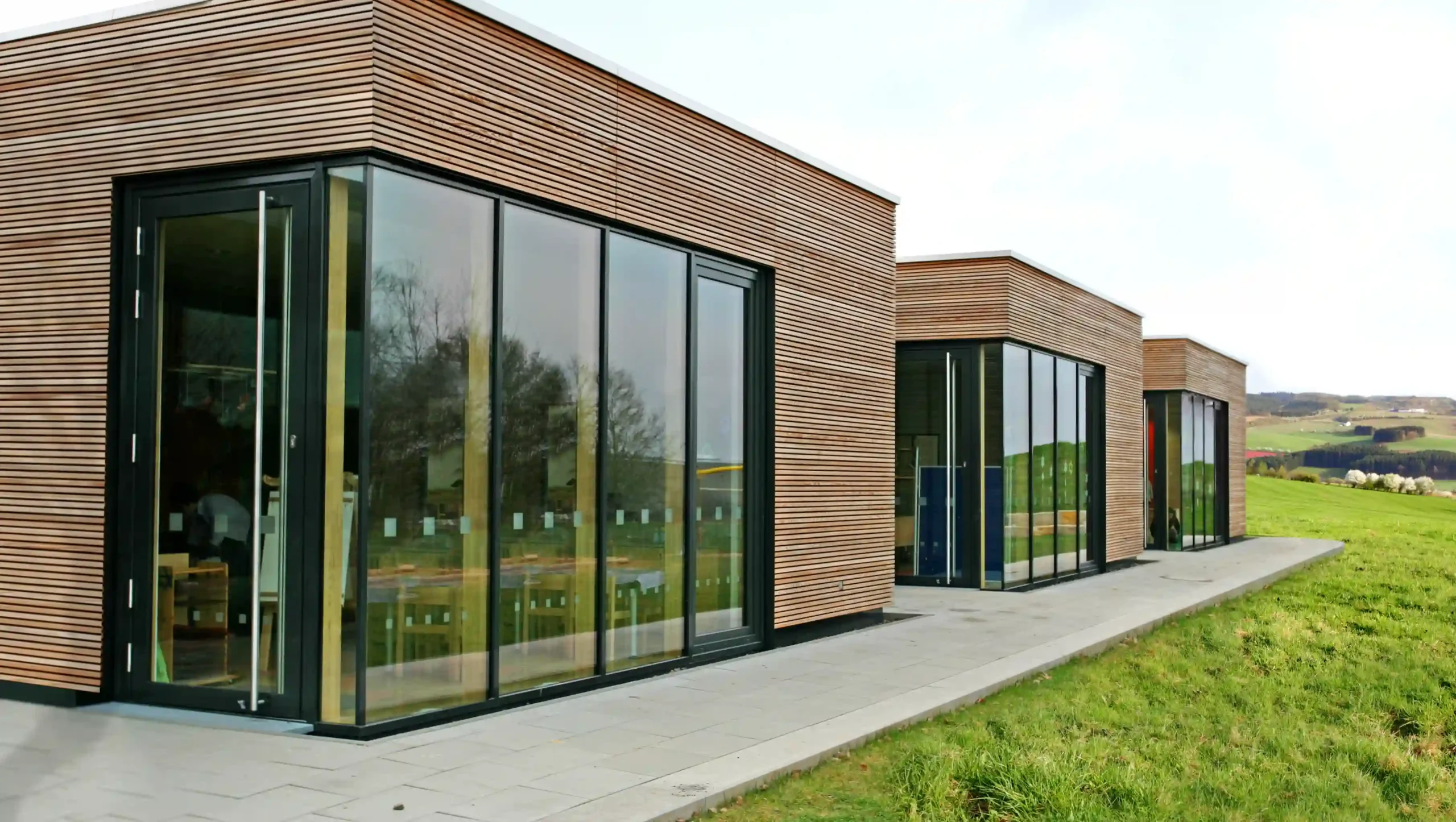 Moderne Holzhäuser auf einer grünen Wiese mit mit großen Holz-Aluminium-Fenstern.