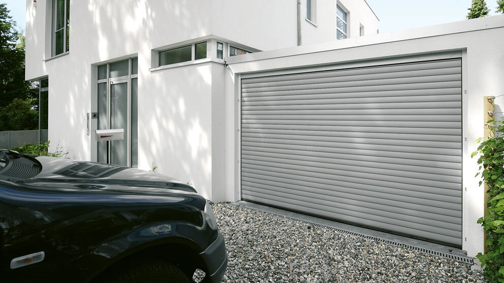 Hellgraues Deckenlauftor an einer angebauten Garage mit geschotterter Auffahrt