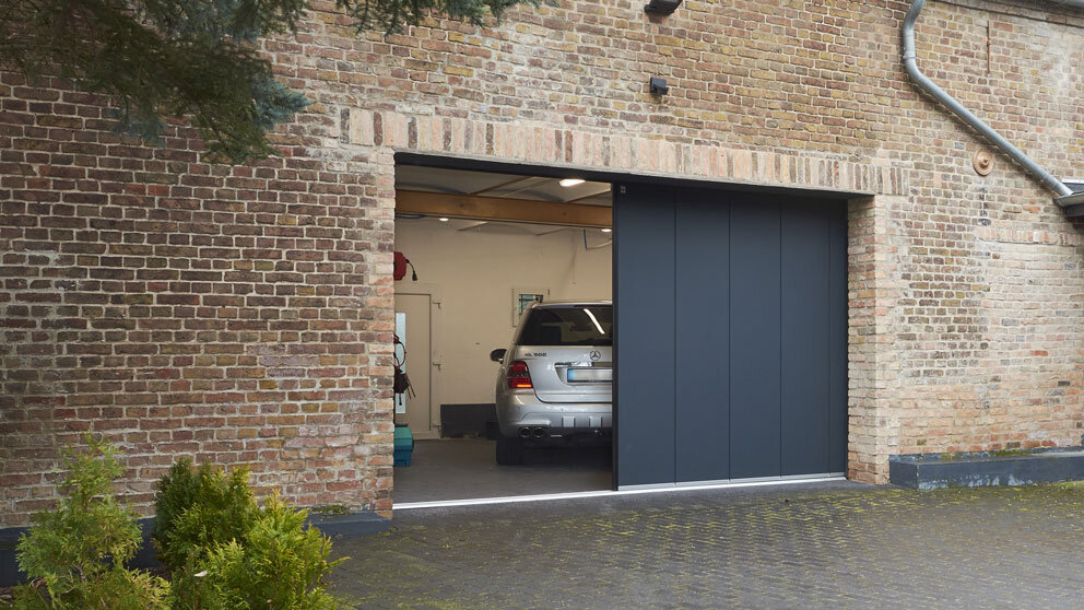Stählernes Seiten-Sektionaltor von außen halb geöffnet mit silbernem Auto in der Garage