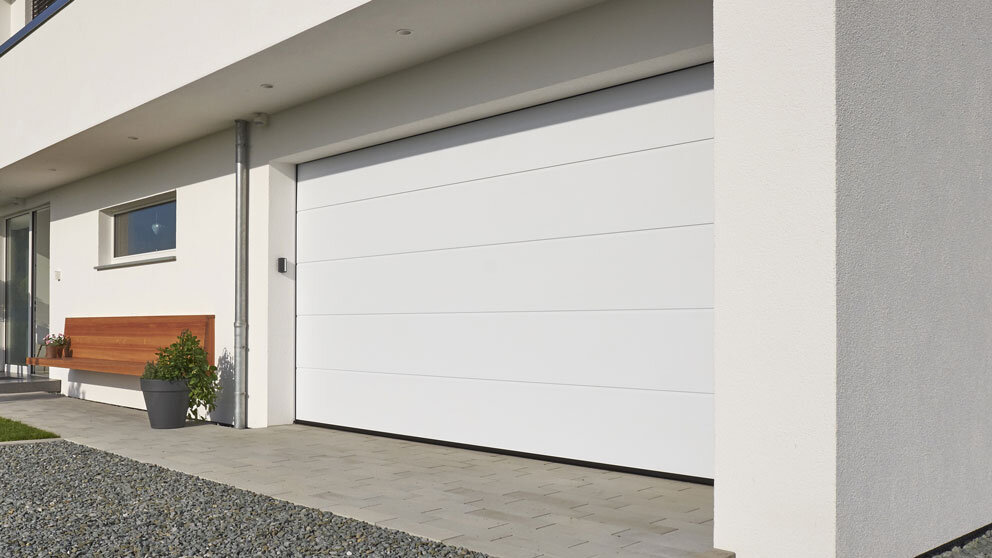 Weißes Steinau Sektionaltor an einer eingebauten Garage mit Bank davor