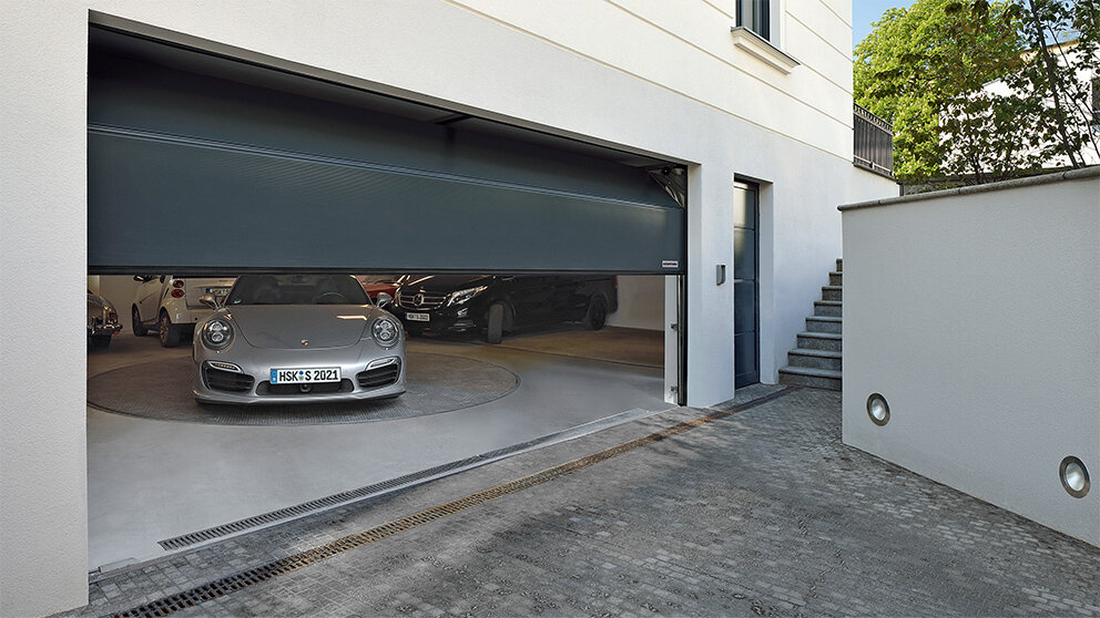 Halb geöffnetes dunkelgraues Steinau Sektionaltor mit teuren Autos in der Garage