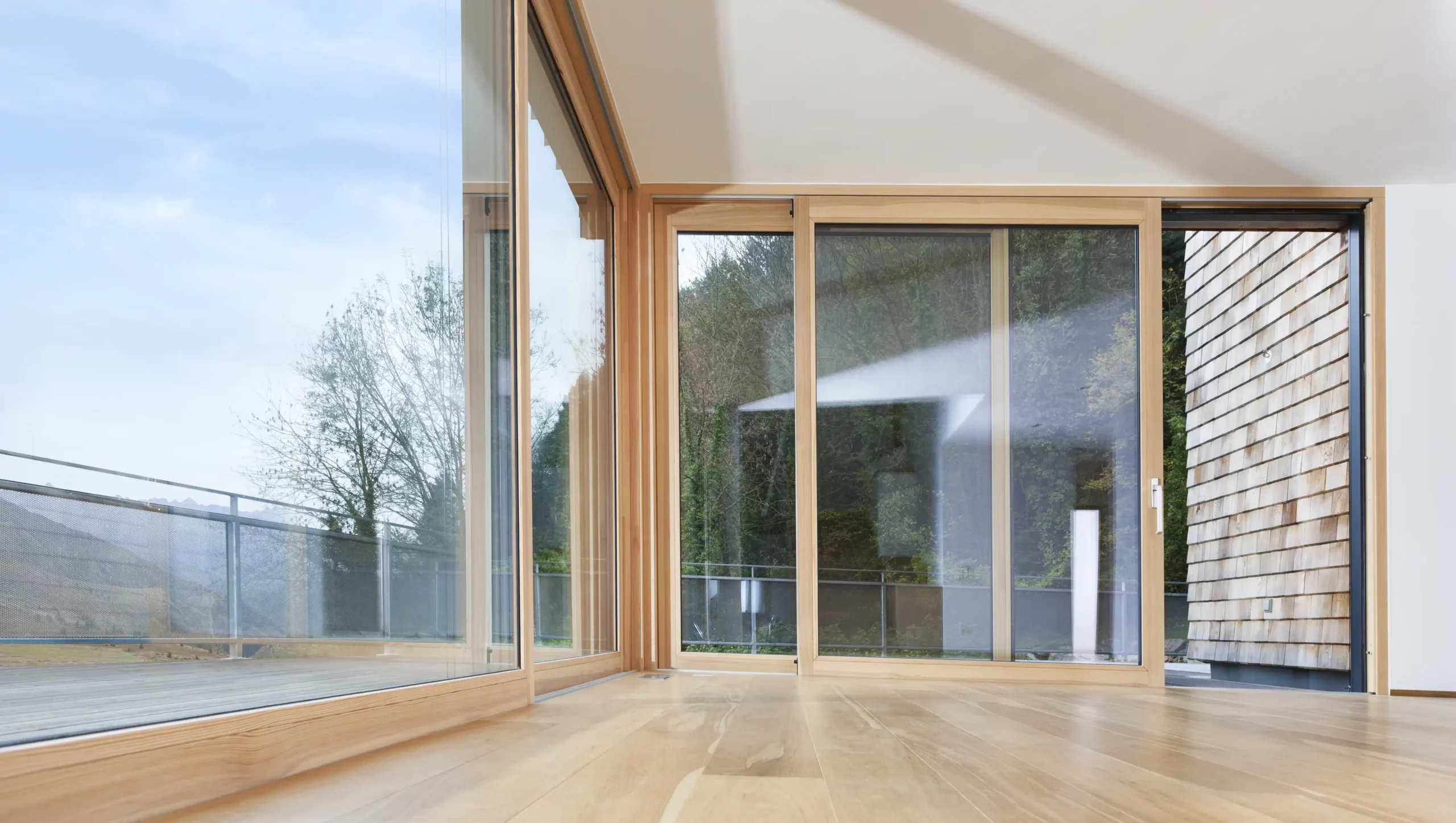 Holz-Aluminium Hebeschiebetüren als große Fensterfront vor einem Balkon.